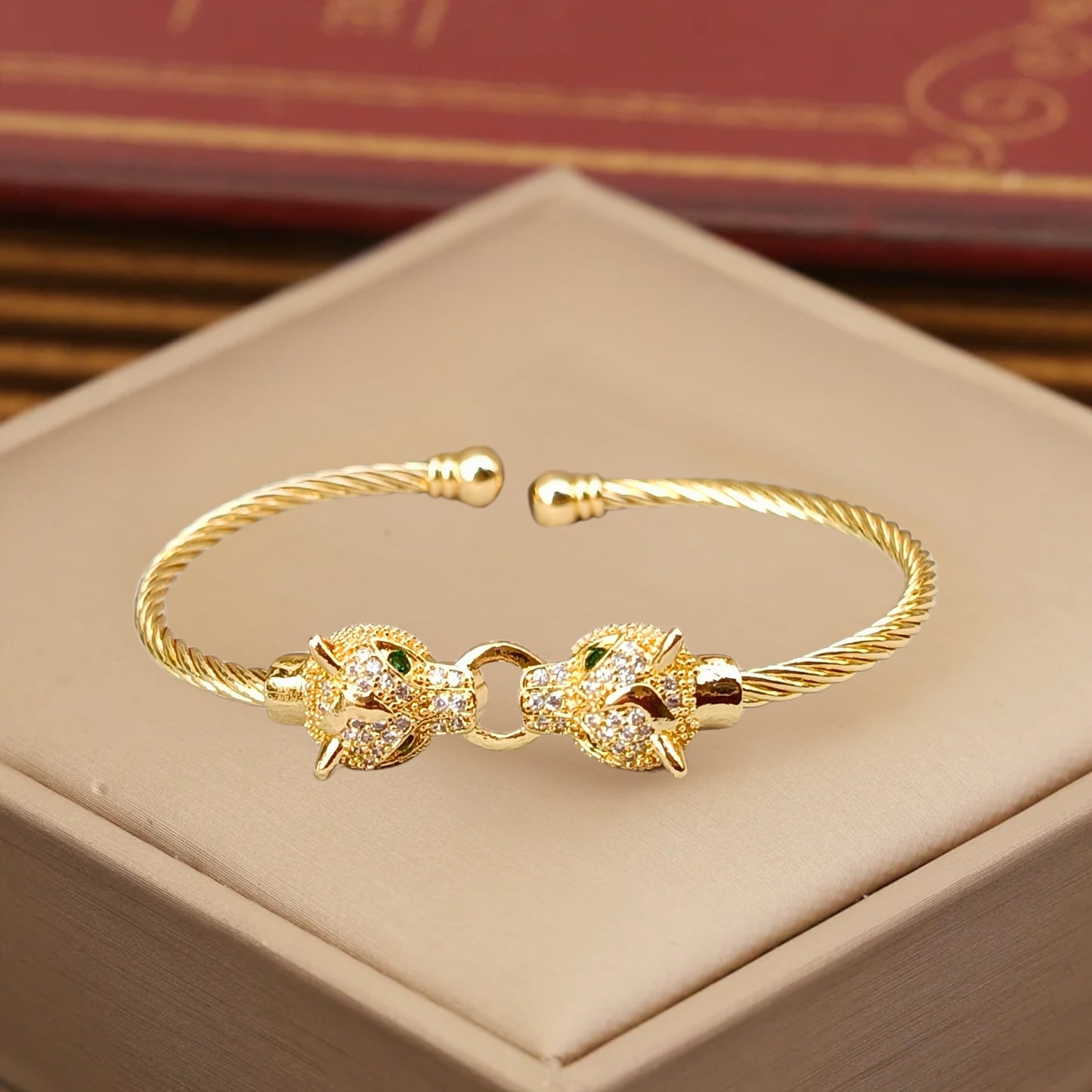 A gold cuff bracelet featuring two detailed jaguar heads with emerald-green eyes