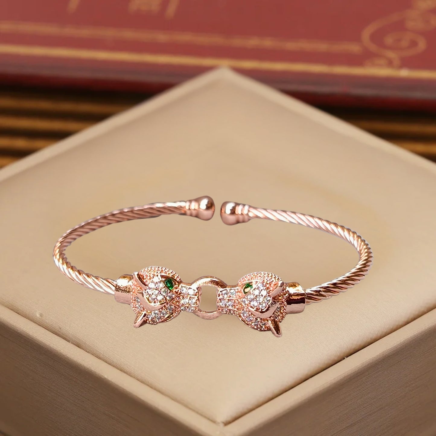 A rose gold cuff bracelet featuring two detailed jaguar heads with emerald-green eyes