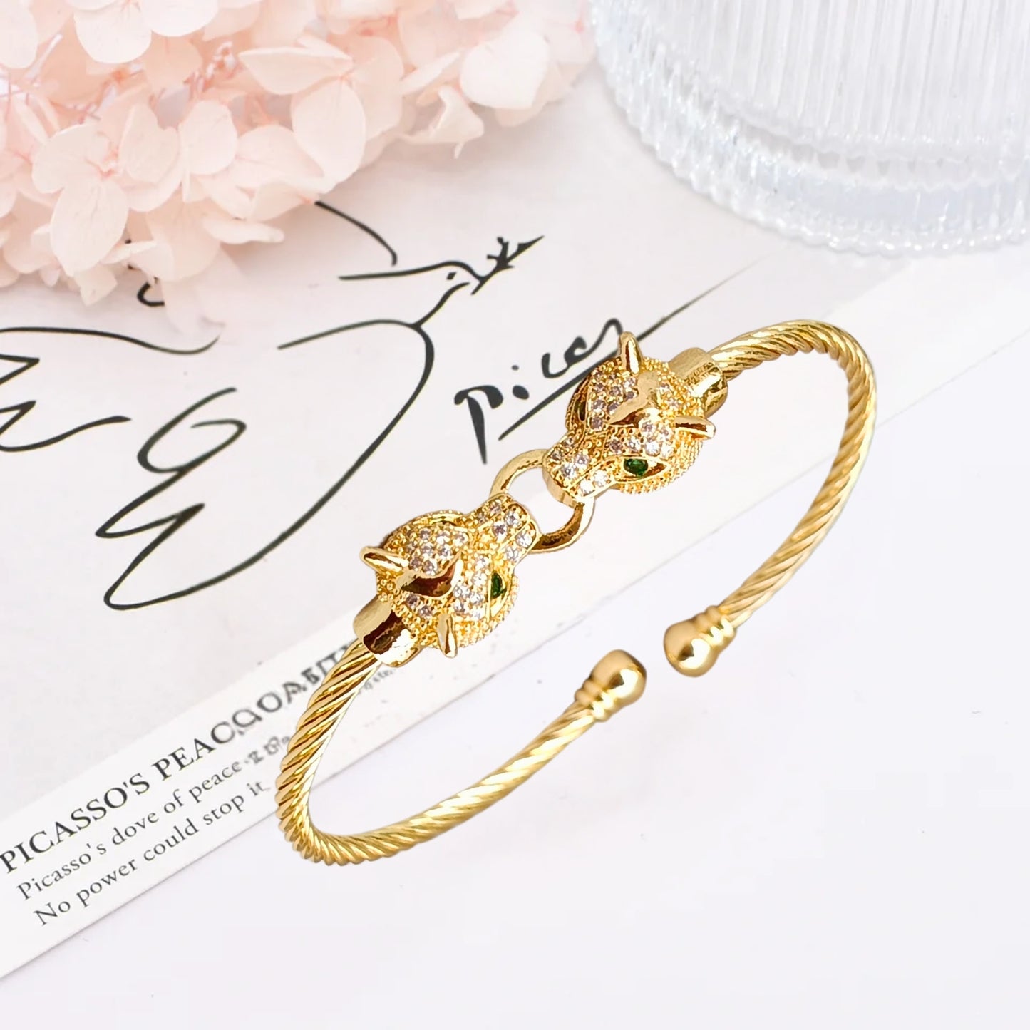 A gold cuff bracelet featuring two detailed jaguar heads with emerald-green eyes