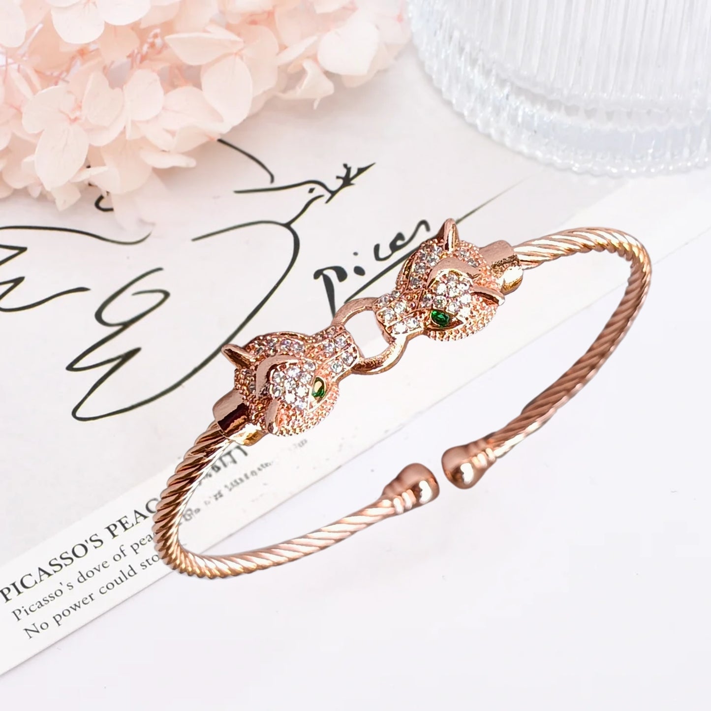 A rose gold cuff bracelet featuring two detailed jaguar heads with emerald-green eyes