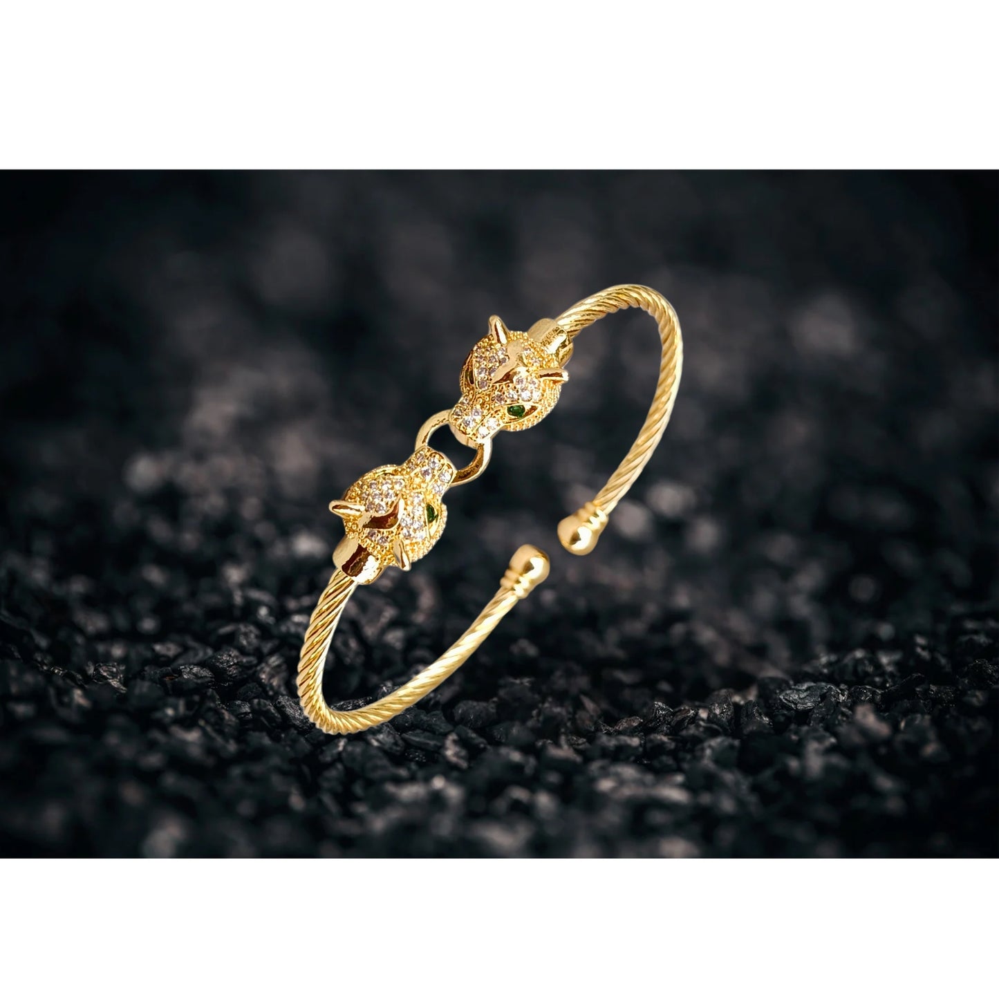 A gold cuff bracelet featuring two detailed jaguar heads with emerald-green eyes