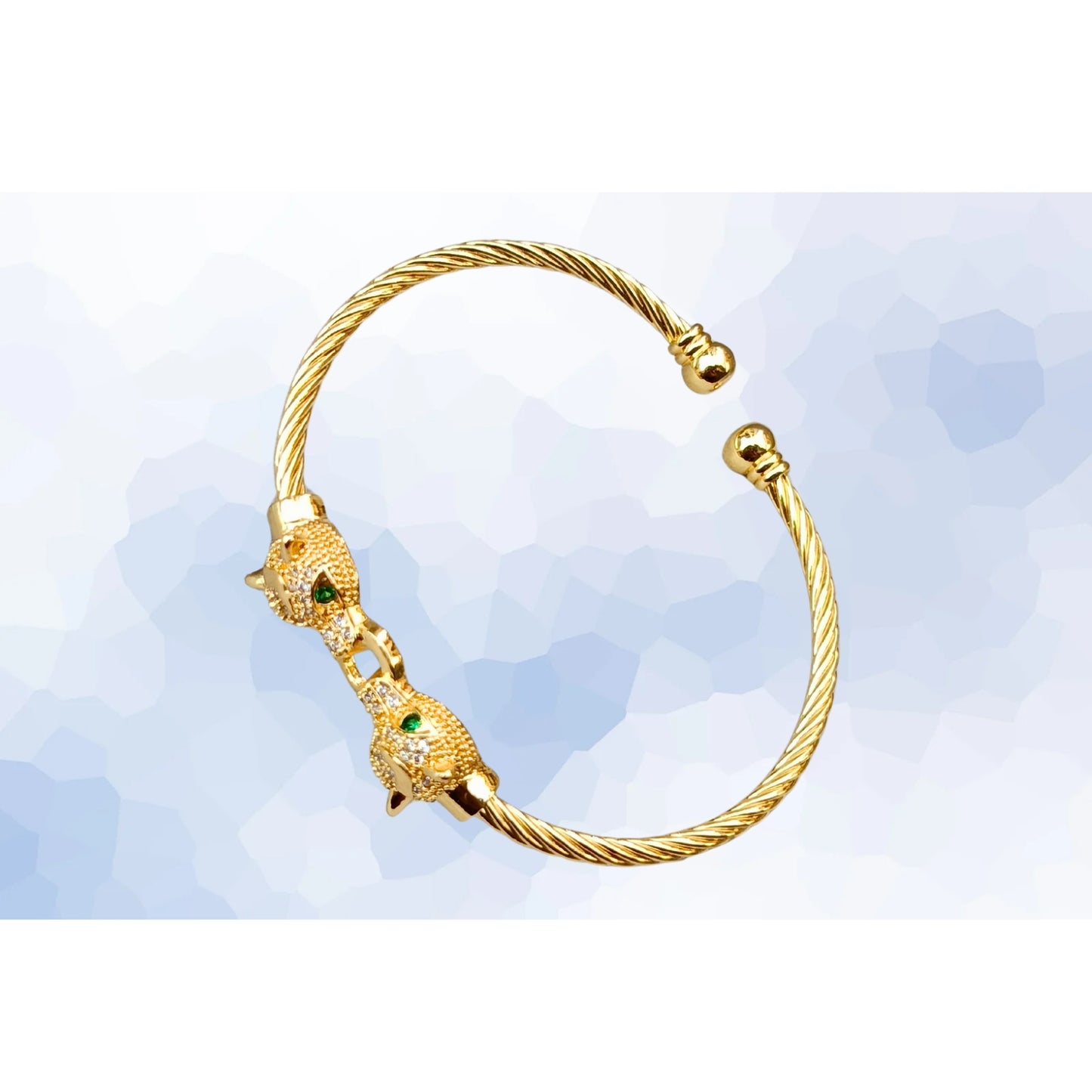 A gold cuff bracelet featuring two detailed jaguar heads with emerald-green eyes