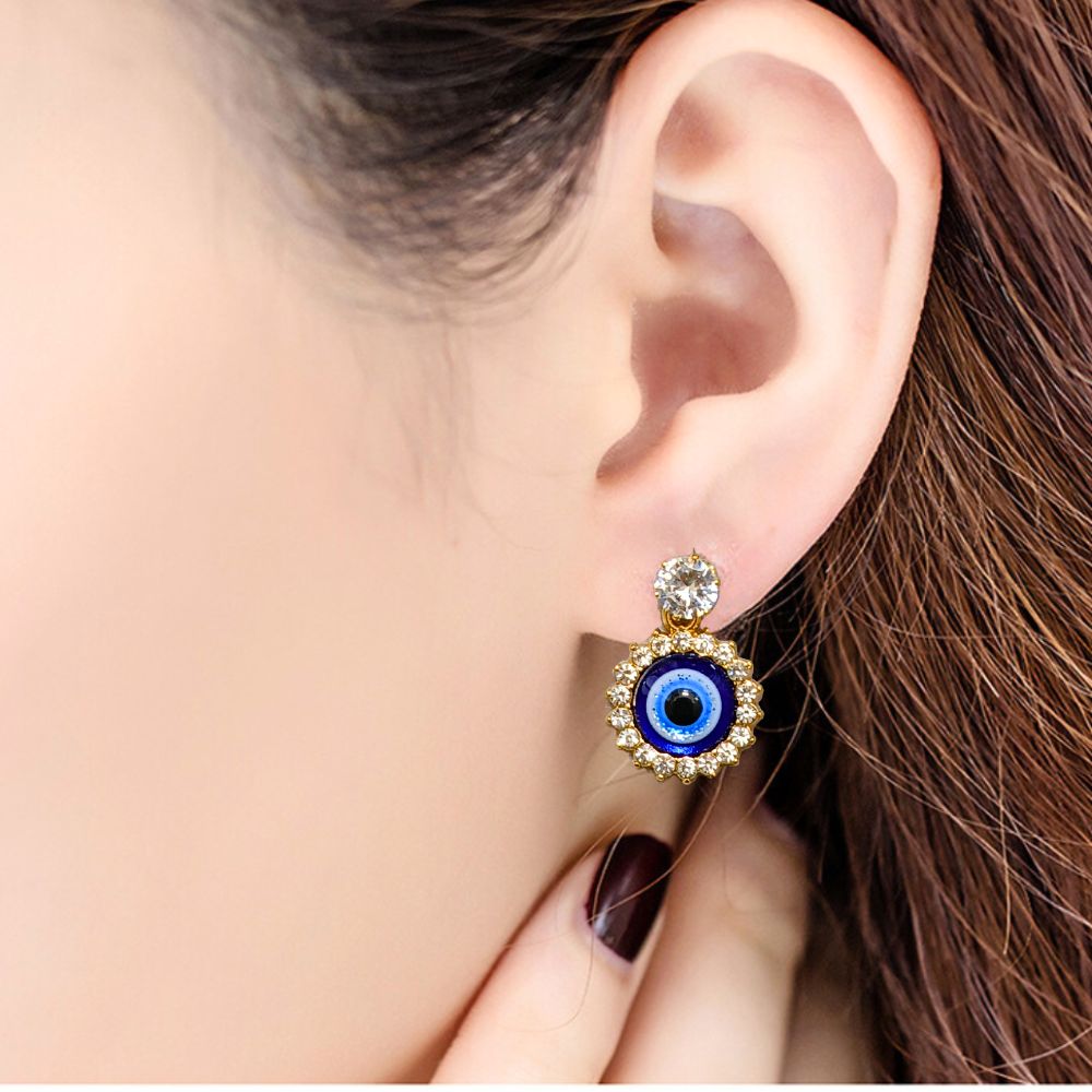 Close-up of gold evil eye earrings with a crystal halo design on a vibrant red fabric background
