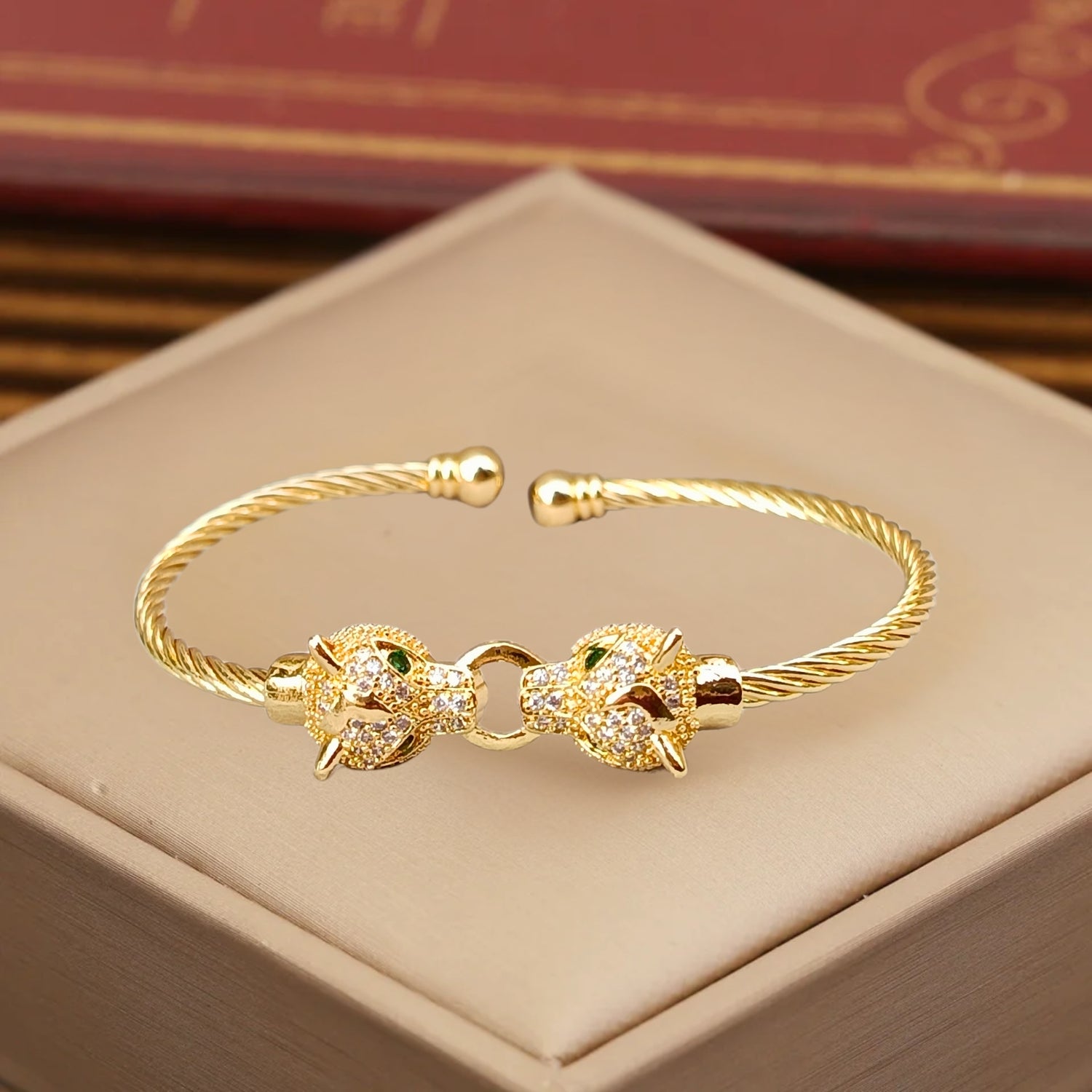 A gold cuff bracelet featuring two detailed jaguar heads with emerald-green eyes