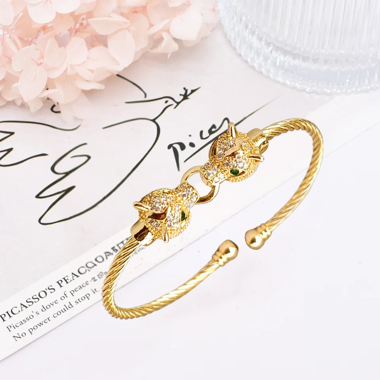 A gold cuff bracelet featuring two detailed jaguar heads with emerald-green eyes